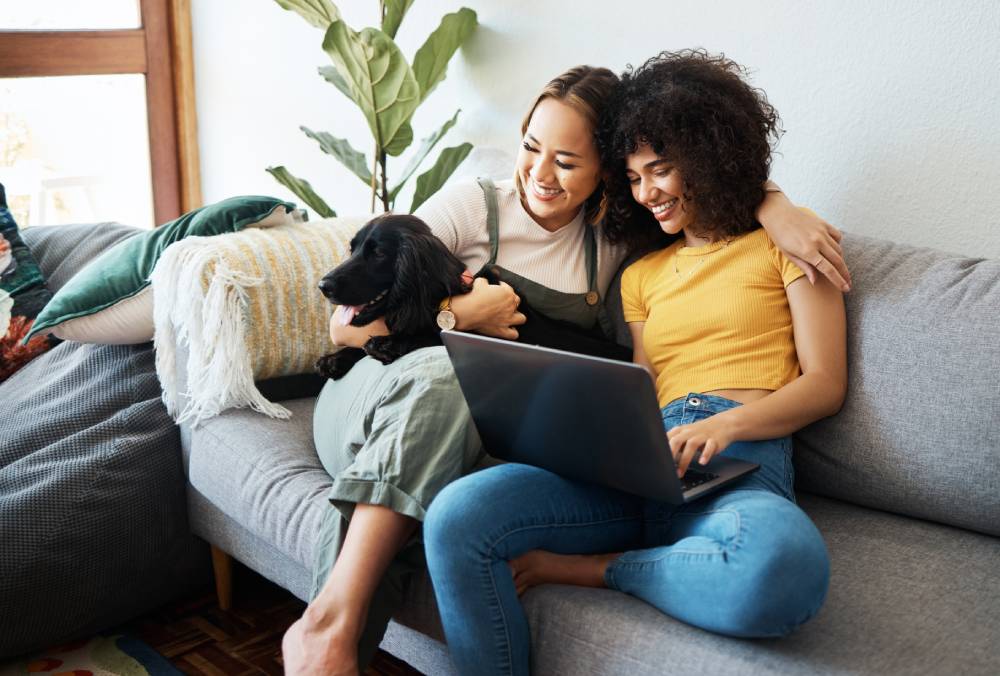Two women relaxing together with a laptop and pet dog | Hemmat Law Group